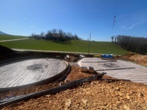 Biogasanlagenbau: Rohbau von Fermenter und Nachfermenter mit sichtbarer Stahlarmierung. Baufortschritt mit Baumaschinen und Materialhaufen.